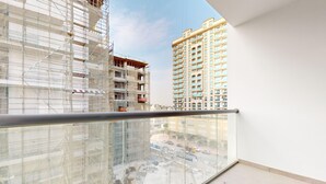 A high-rise building with a glass balcony, construction scaffolding, and a clear view of the surrounding urban landscape. - Modern Furnished Studio in Uniestate Supreme (Dubai)