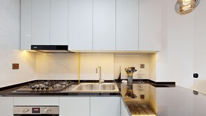 A modern kitchen with a gas stove, stainless steel sink, and white cabinetry. - Modern Furnished Studio in Uniestate Supreme (Dubai)