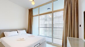 A modern hotel room with a large bed, a glass partition window, and a view of the cityscape. - Modern Furnished Studio in Uniestate Supreme (Dubai)