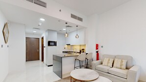 A modern living room with a sofa, a round coffee table, and a kitchen area with a central island. - Modern Furnished Studio in Uniestate Supreme (Dubai)