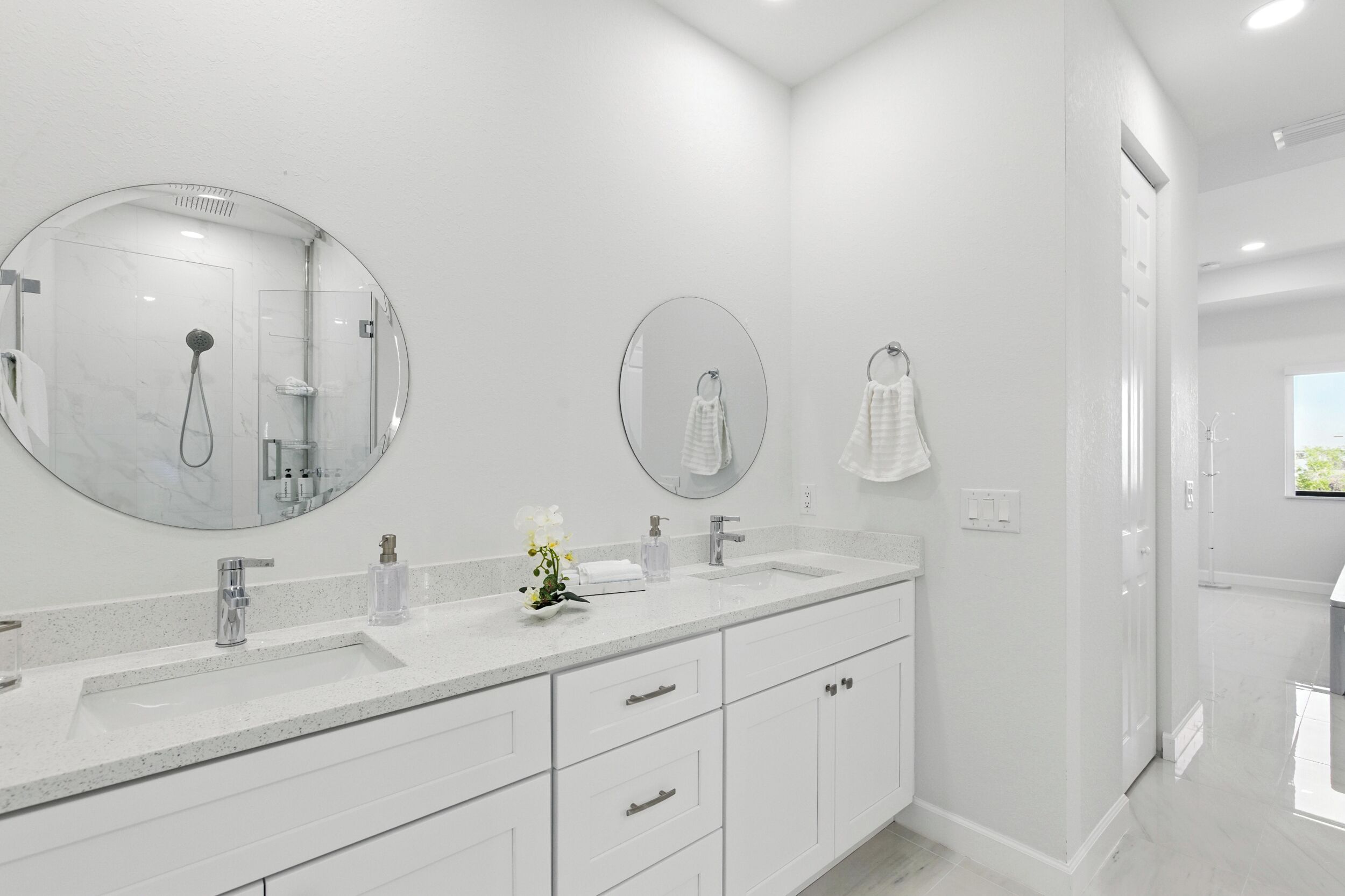 A modern bathroom with a large mirror, two sinks, and a shower.