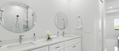 A modern bathroom with a large mirror, two sinks, and a shower.