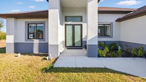 Una casa moderna con techo plano, entrada central con puertas de vidrio y un pequeño jardín.