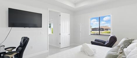 Un dormitorio moderno con una cama grande, un televisor de pantalla plana en la pared, un escritorio con una silla y un ventanal con vistas al exterior.