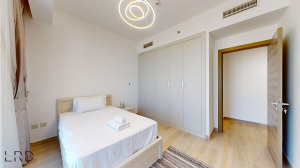A bedroom with a bed, a wardrobe, a bedside table, and a door leading to another room.