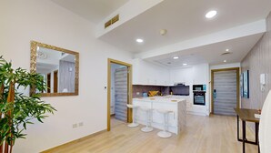 A modern kitchen with white cabinets, a central island with bar stools, and a dining area with a table and chairs. - Stylish Retreat with Scenic Views in Bloom Towers (Dubai)