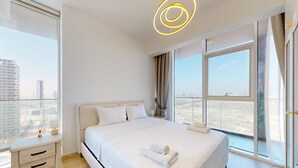 A modern hotel room with a large bed, a bedside table, a nightstand, and a view of the cityscape through large windows. - Stylish Retreat with Scenic Views in Bloom Towers (Dubai)