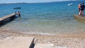 A pebbled beach with clear water, boats, and people. - Seaside Garden Villa Kožino (Kožino)
