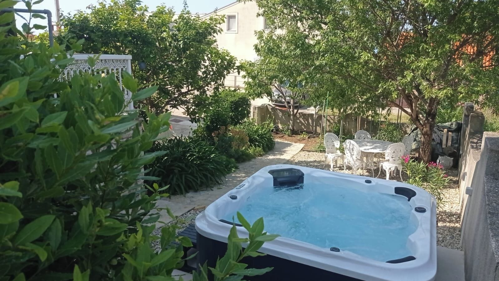 Een hottub in een achtertuin, omringd door groen, met een gebouw op de achtergrond.