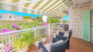 A covered outdoor area with wicker furniture, potted plants, and a view of the surrounding buildings. - Seaside Garden Villa Kožino (Kožino)