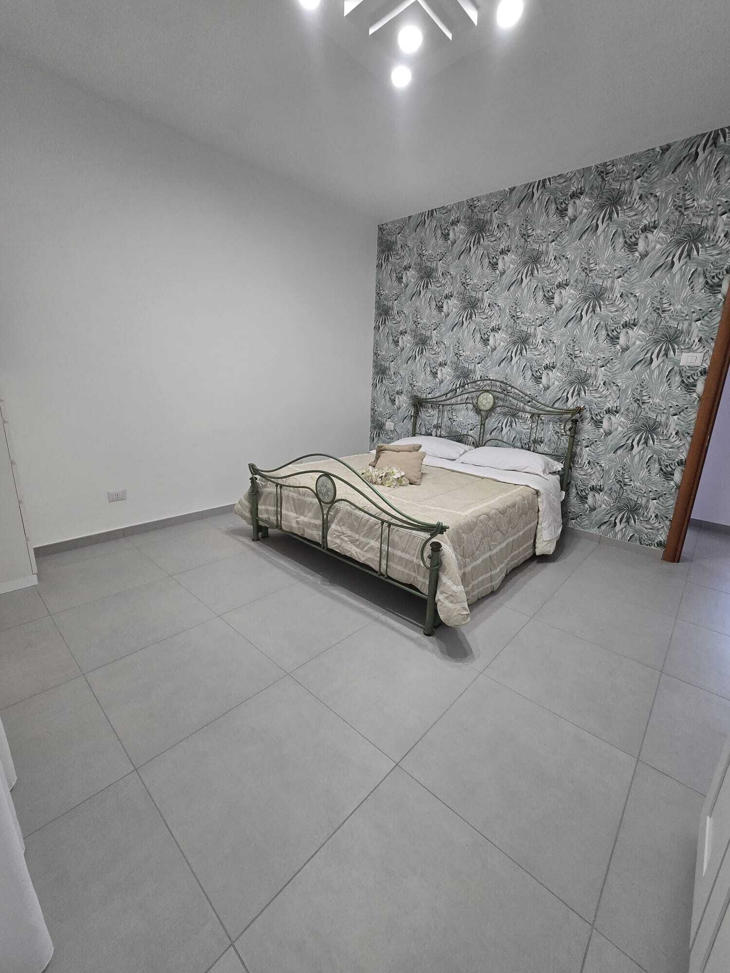 Un dormitorio con cama, paredes blancas y papel tapiz floral.