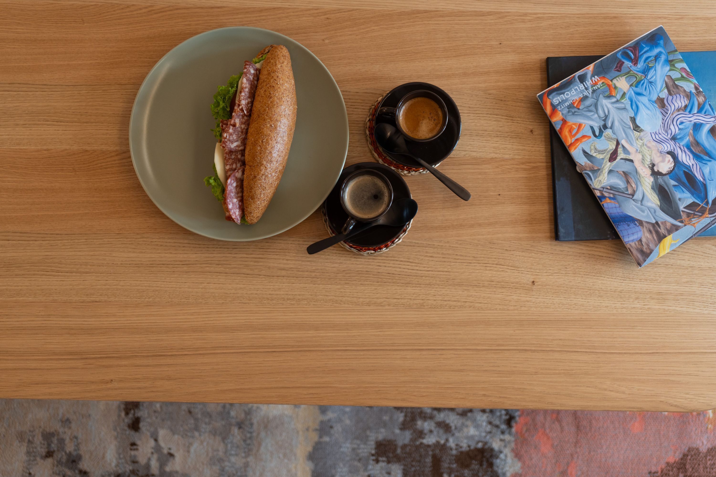 Un sandwich sur une assiette, deux tasses de café et un livre sur une table.