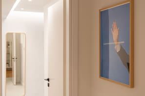 A modern room with a framed artwork of a hand reaching towards a horizontal line, a door with a black handle, and a mirror reflecting a bathroom. - LIV - Modern Heavenly Retreat in Exarcheia (Athens)
