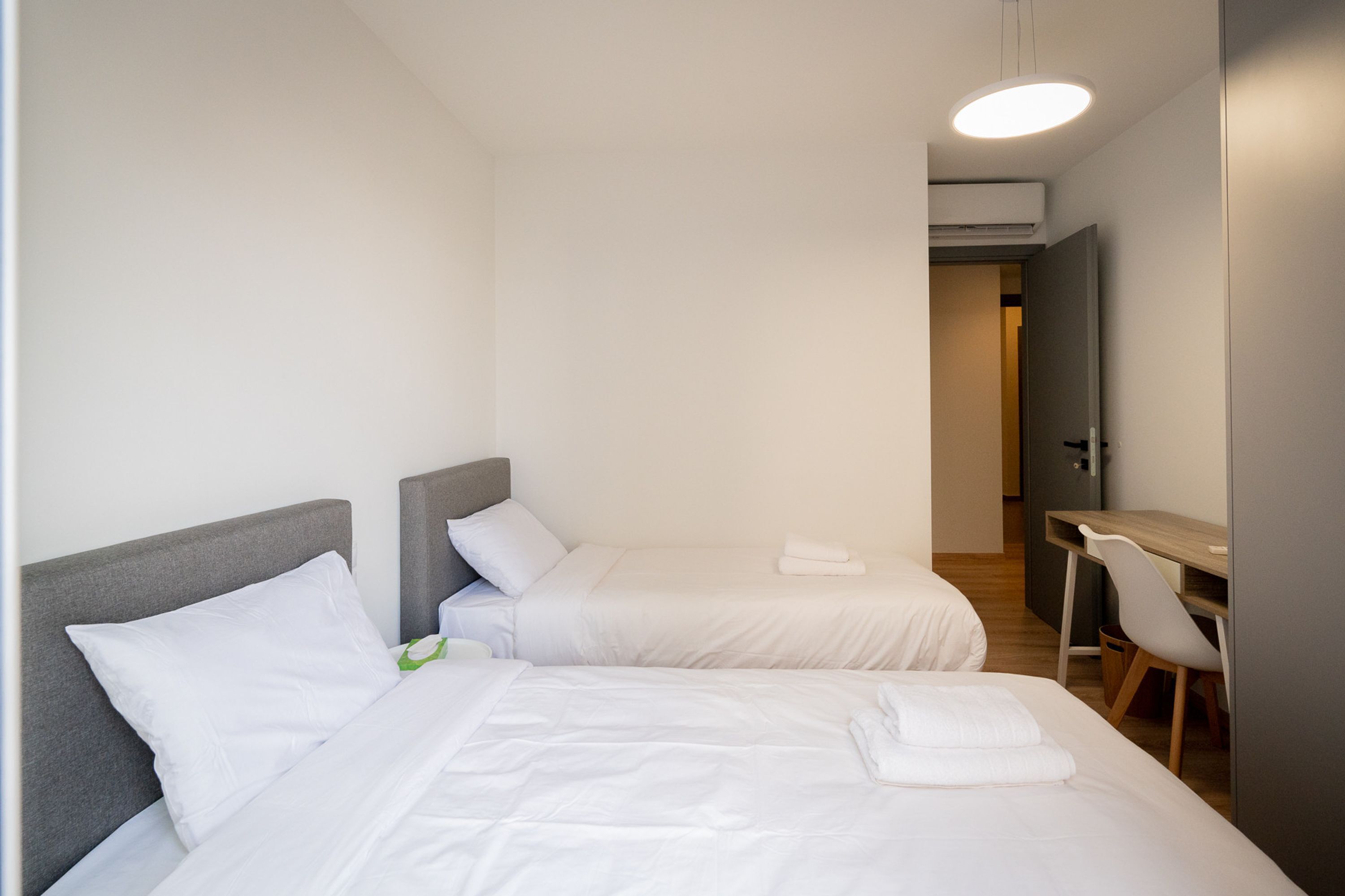 A hotel room with two single beds, a desk, and a chair.