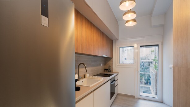 A modern kitchen with a built-in oven, a sink, and a window overlooking a balcony. - LIV - Captivating Apartment in Pagrati (Athens)