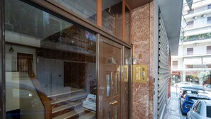 L'ingresso di un hotel con una porta in vetro, gradini in marmo e sullo sfondo auto parcheggiate e edifici.