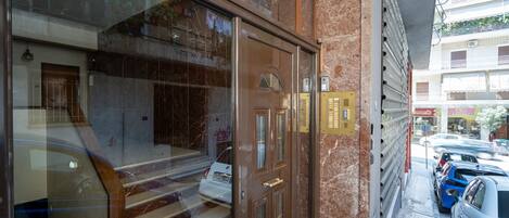 A hotel entrance with a glass door, marble steps, and a view of parked cars and buildings in the background.