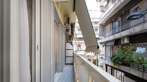 Un balcone stretto con ringhiera metallica, condizionatori e vista sugli edifici limitrofi.