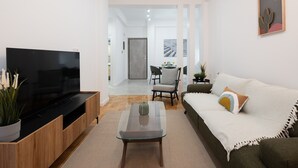 Un soggiorno moderno con televisore a schermo piatto, mobile TV in legno, tavolino in vetro e un divano accogliente con una coperta.