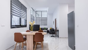 A modern, well-lit room with a dining table, chairs, and a sofa. - LIV - Modern Spacious Apartment in Gazi (Athens)