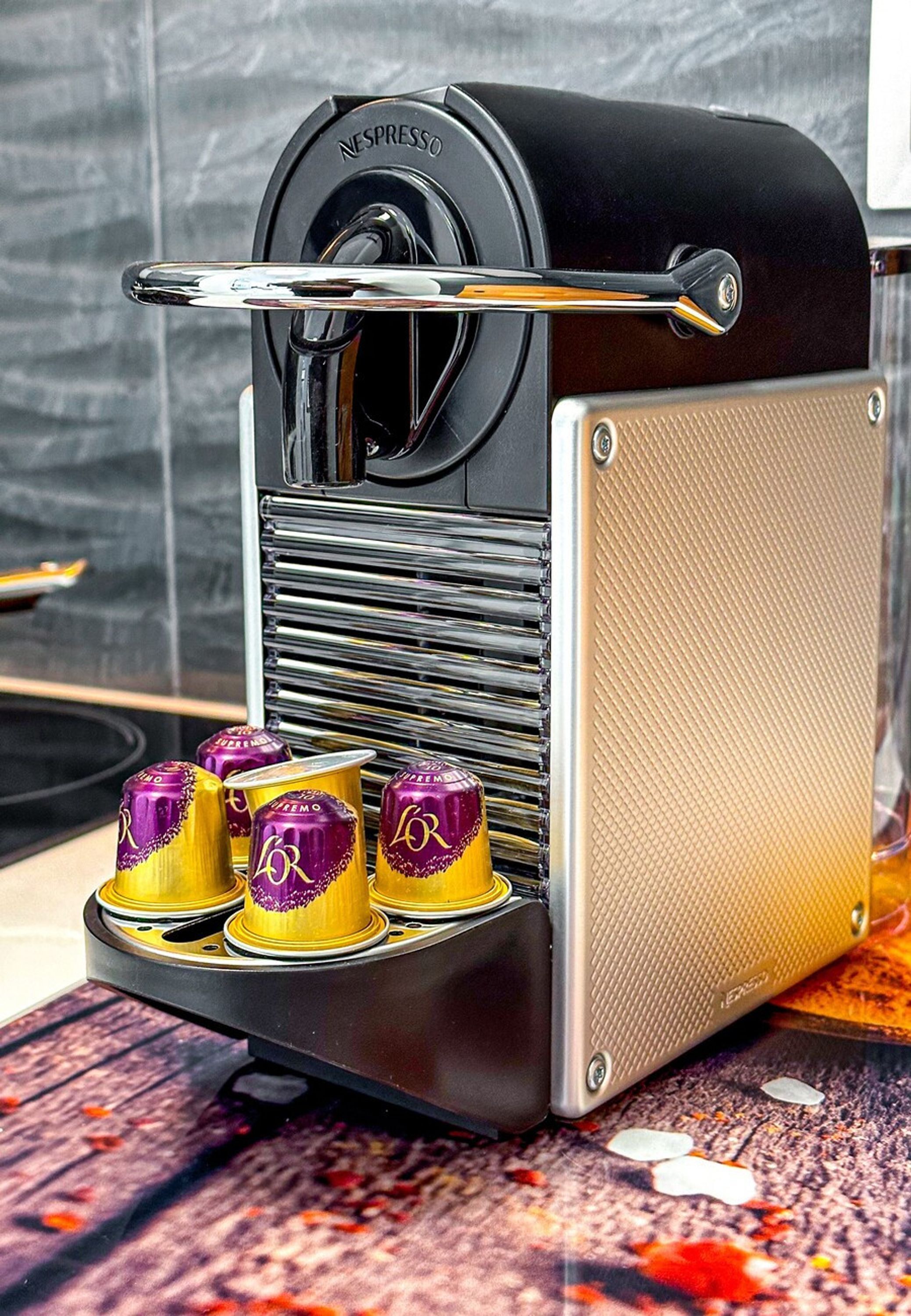 A coffee machine with a black and beige design, a coffee cup holder, and four coffee cups with a purple and gold design.