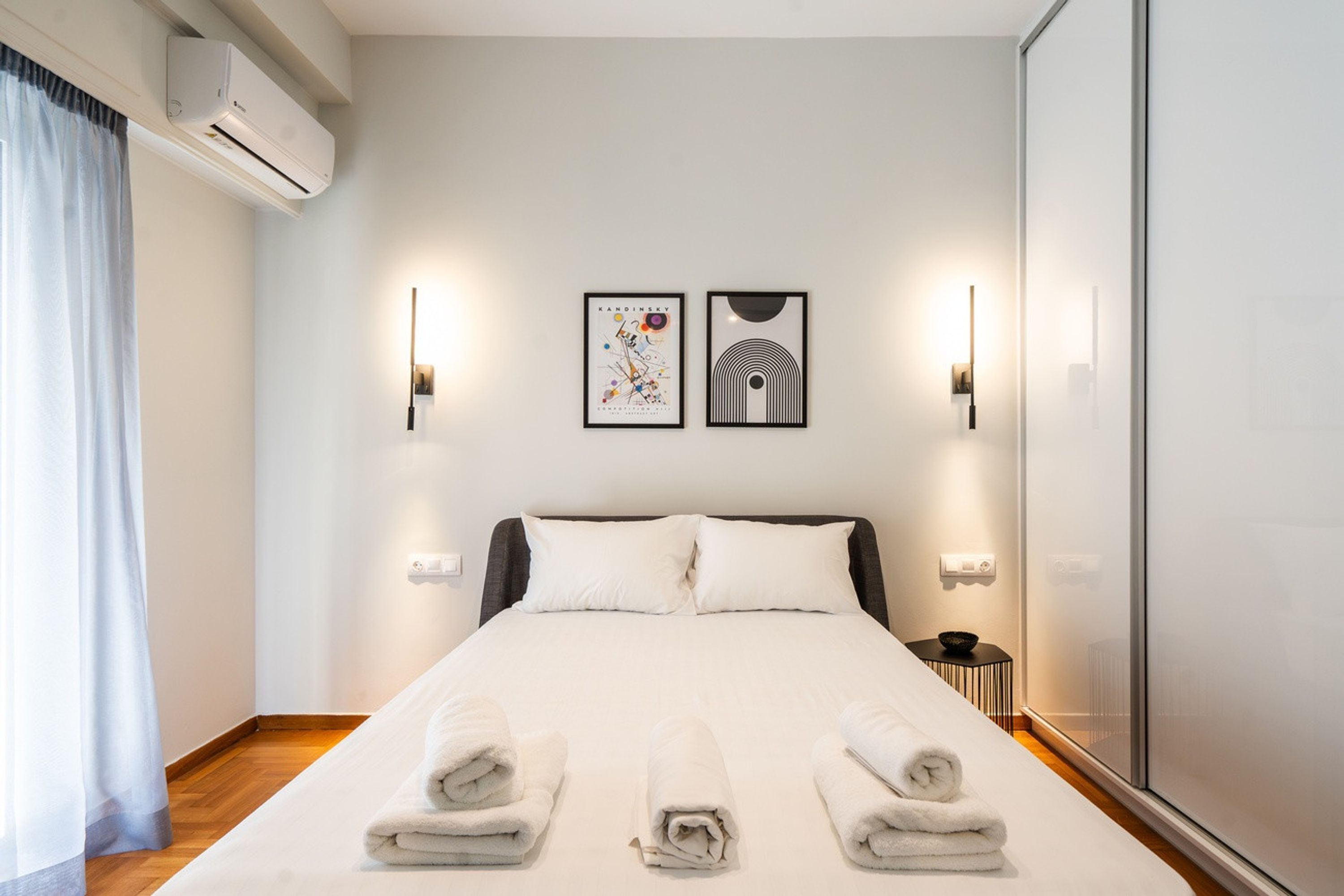 A hotel room with a bed, two wall-mounted lights, a framed artwork, and a small table with a bowl.