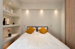 Ein Schlafzimmer mit einem Bett, weißen Wänden, einer Holztür und Regalen mit Dekoration.