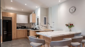 A modern kitchen with wooden cabinets, a marble countertop island, and grey bar stools. - LIV - Cozy Urban Apartment in Pagrati (Athens)