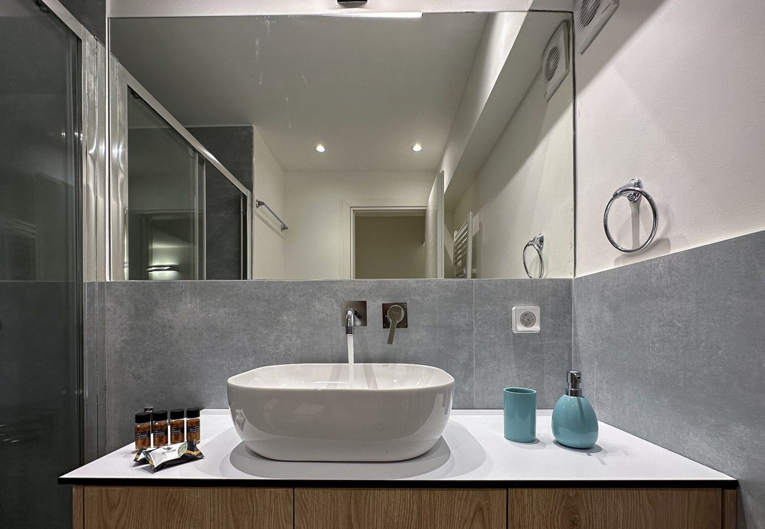 Ein modernes Badezimmer mit einem großen, ovalen Waschbecken, einem Spiegel und einer sichtbaren Dusche im Hintergrund.