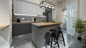 A modern kitchen with grey cabinets, a wooden countertop, a built-in island with stools, and a pendant light. - LIV - Modern Comfort Oasis in Pagrati (Kaisariani)