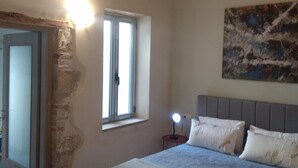 A bedroom with a bed, a nightstand, a window, and a painting on the wall.