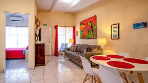 A hotel room with a bed, a sofa, a dining table with chairs, a lamp, and a painting on the wall. - Villas Paraiso B52 (Jacó)