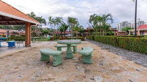 A stone patio with a round table and benches, surrounded by palm trees and a hedge. - Villas Paraiso B52 (Jacó)