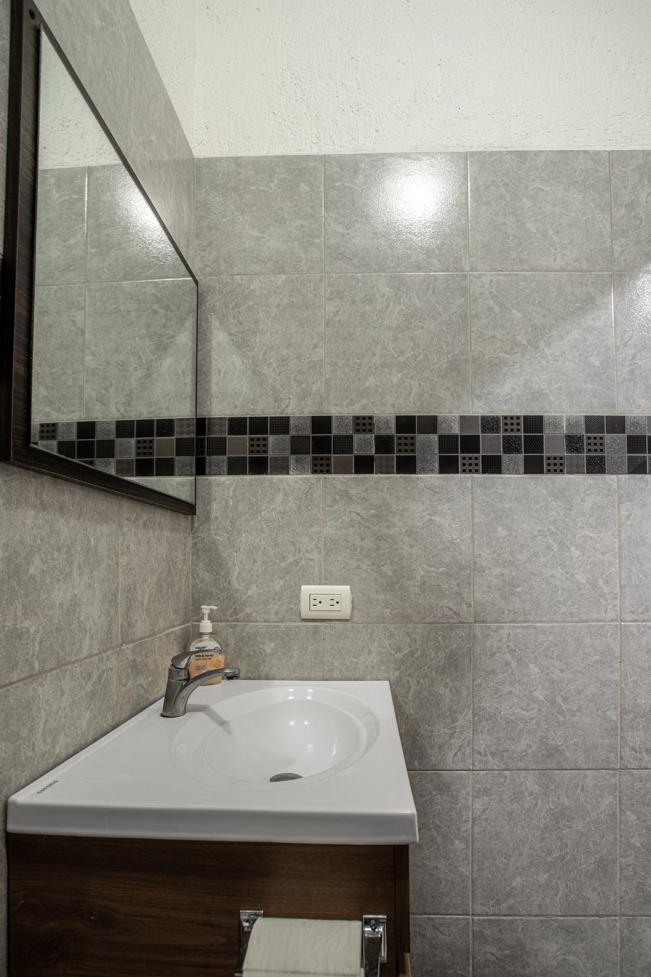 A bathroom with a white sink, dark wooden cabinet, and a tiled backsplash.