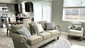 A living room with a beige sofa, a patterned rug, and a view of the outdoors through a window.