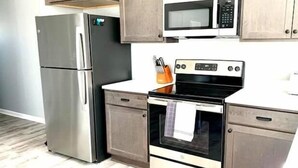 A kitchen with a stainless steel refrigerator, a microwave, an oven, and wooden cabinets.