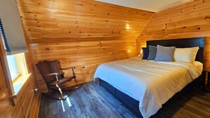 Een houten slaapkamer met een bed, een stoel en een nachtkastje met een lamp.