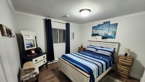 Une chambre à coucher comprenant un lit, des tables de chevet, un bureau avec une chaise, une fenêtre avec des rideaux et des œuvres d’art accrochées au mur.