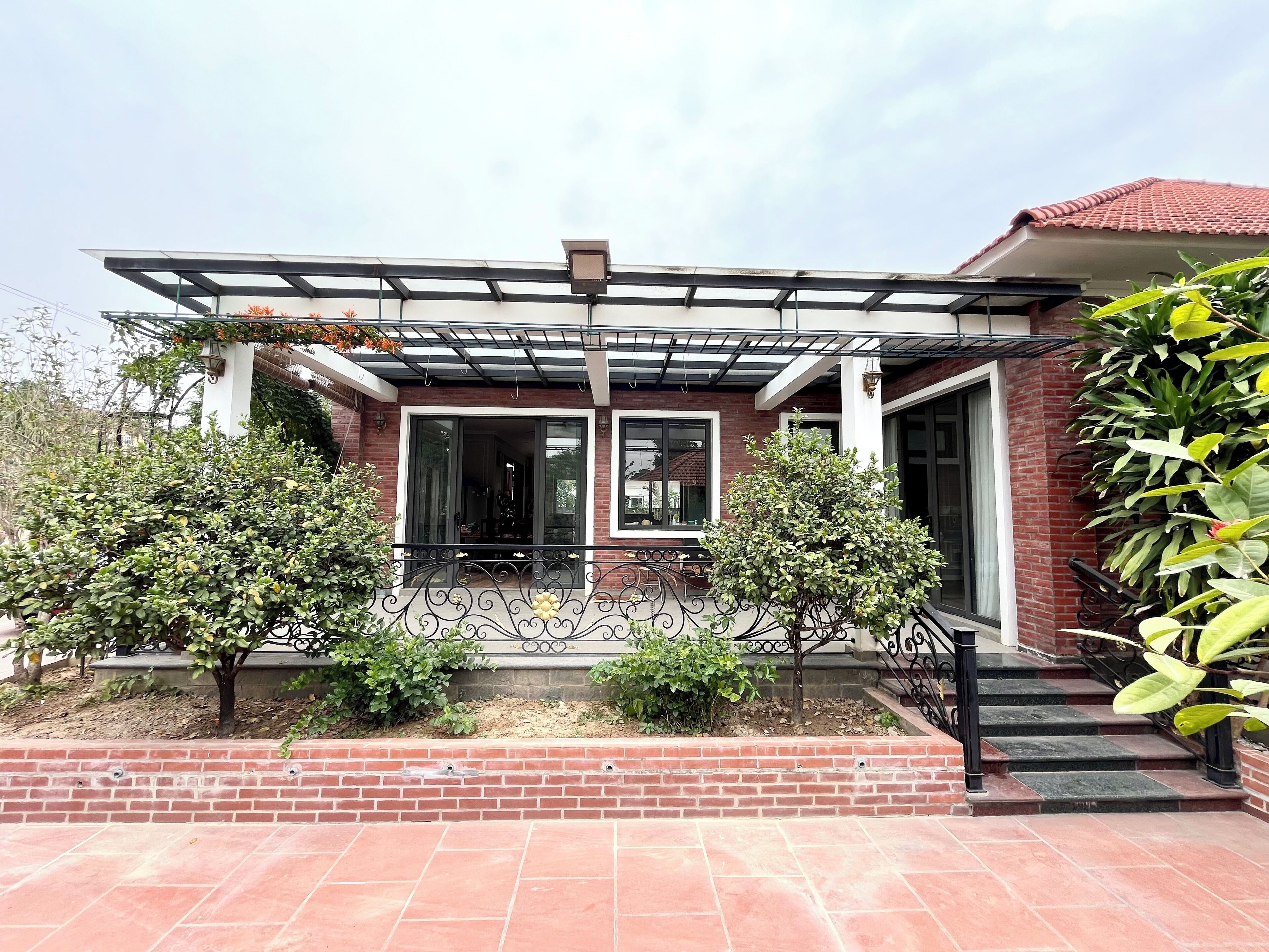 A house with a covered porch, a brick exterior, and a small garden area with steps leading to the entrance.