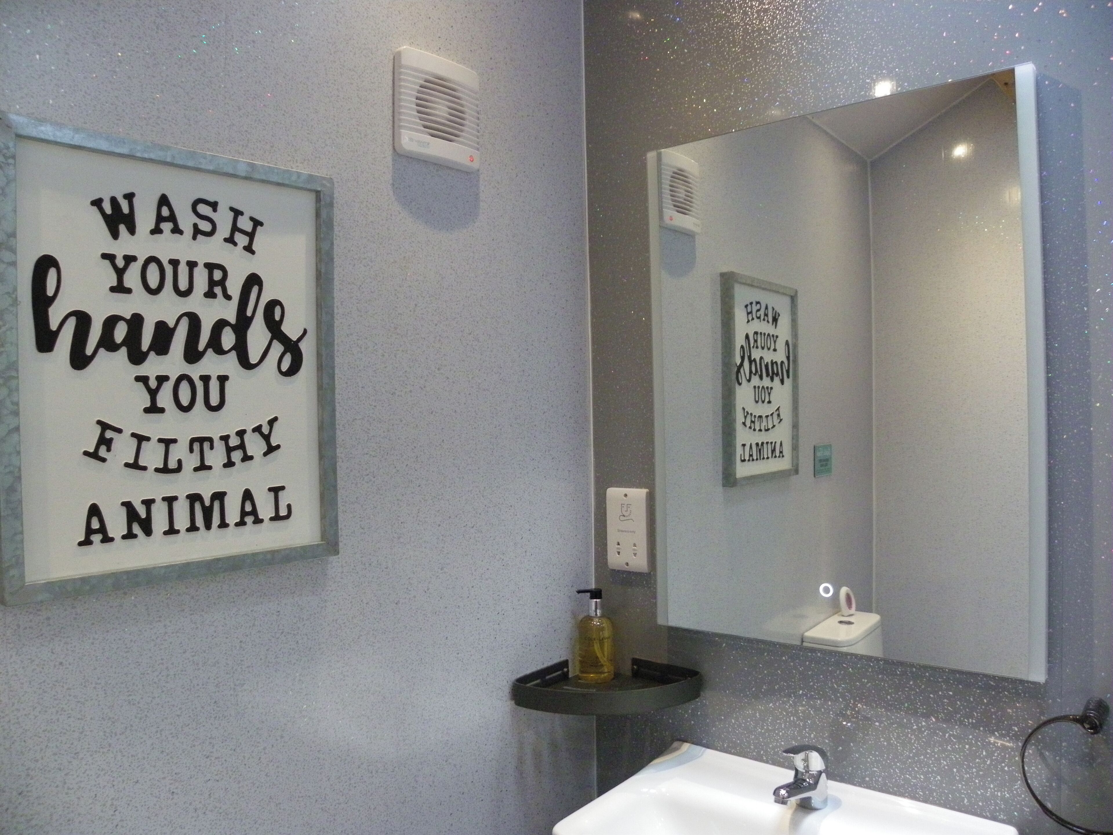 A bathroom with a sink, mirror, and a sign that reads "WASH YOUR HANDS YOU FILTHY ANIMAL".