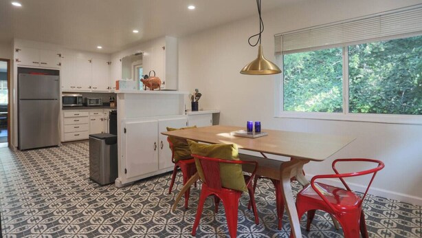 Una cocina moderna con armarios blancos, un refrigerador de acero inoxidable y un comedor con mesa de madera y sillas rojas.
