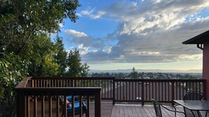 A wooden deck with a table and chairs, overlooking a landscape with distant mountains and a cloudy sky. - Charming 3 BR Home Near Redwood Park w/ Bay Views (Oakland)
