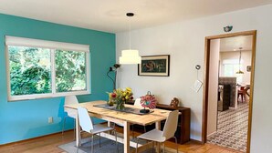 A dining area with a wooden table, white chairs, a vase with flowers, and a pendant light. - Charming 3 BR Home Near Redwood Park w/ Bay Views (Oakland)