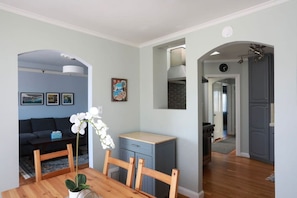 A modern living room with a sofa, dining table, and chairs, a small kitchen area, and a hallway leading to another room.