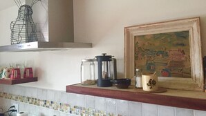 Una cocina con salpicadero de azulejos, estufa a gas, cafetera y un cuadro enmarcado en la pared.