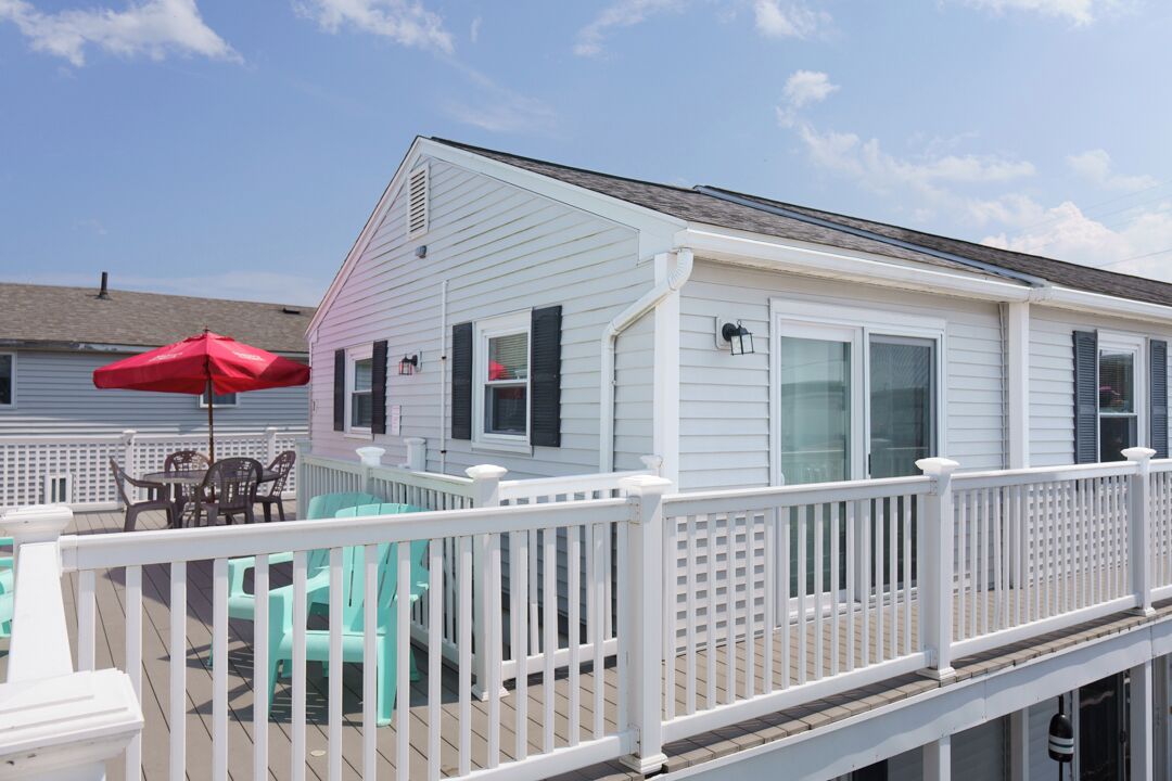 A white house with a deck, a red umbrella, and turquoise chairs.