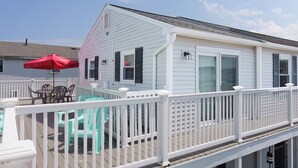 A white house with a deck, a red umbrella, and turquoise chairs. - Beach Bum Hideaway - Cozy studio condo with full kitchen. 400 ft to the beach! (Hampton)