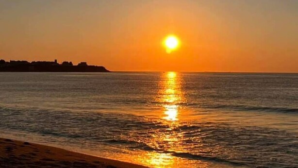 A sunset over a calm sea with a silhouette of a distant shoreline. - Beach Bum Hideaway - Cozy studio condo with full kitchen. 400 ft to the beach! (Hampton)
