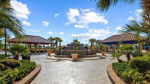 A courtyard with a central fountain, surrounded by covered seating areas and palm trees.