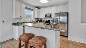 A modern kitchen with white cabinets, a granite countertop, stainless steel appliances, and two woven stools.